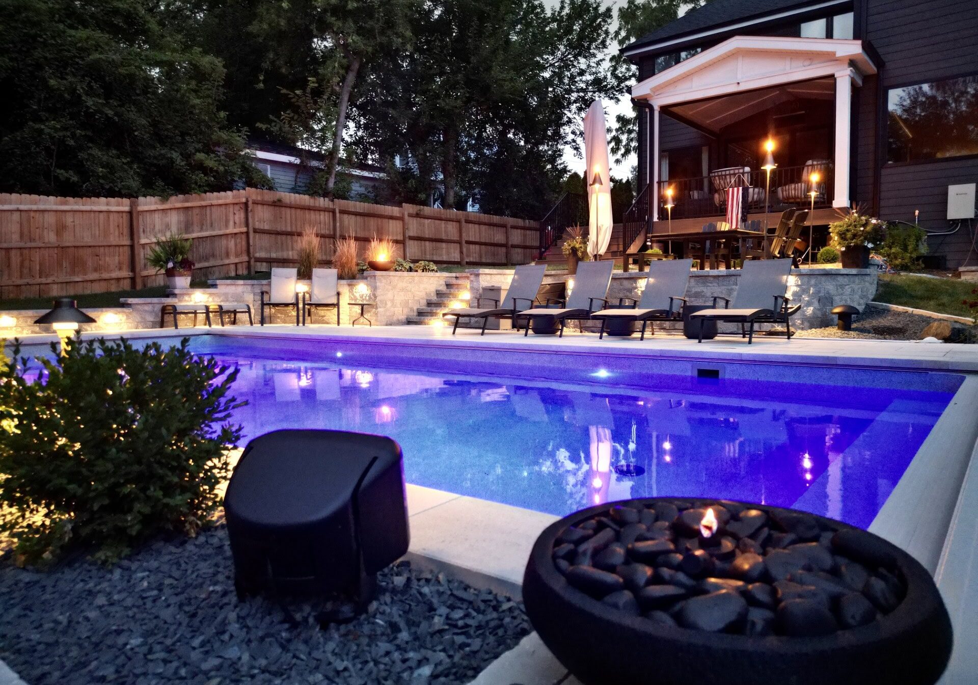 Backyard pool with loungers and patio lighting.