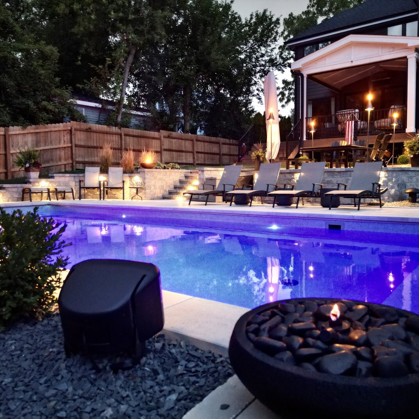 Backyard pool with loungers and patio lighting.
